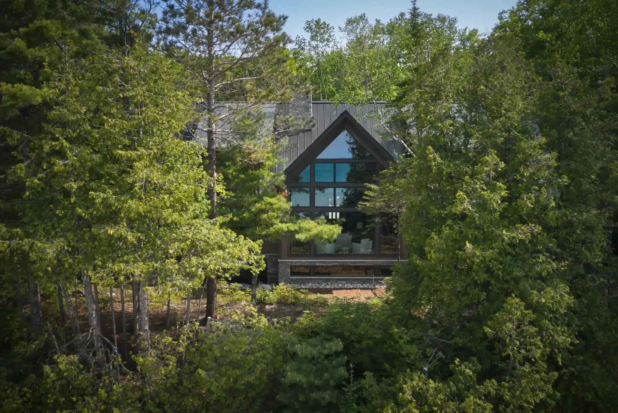 Dark standing seam metal roof on a wooded A-frame home in Northport MI